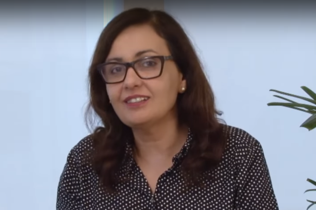 Stela usa óculos, olha para frente e sorri. 