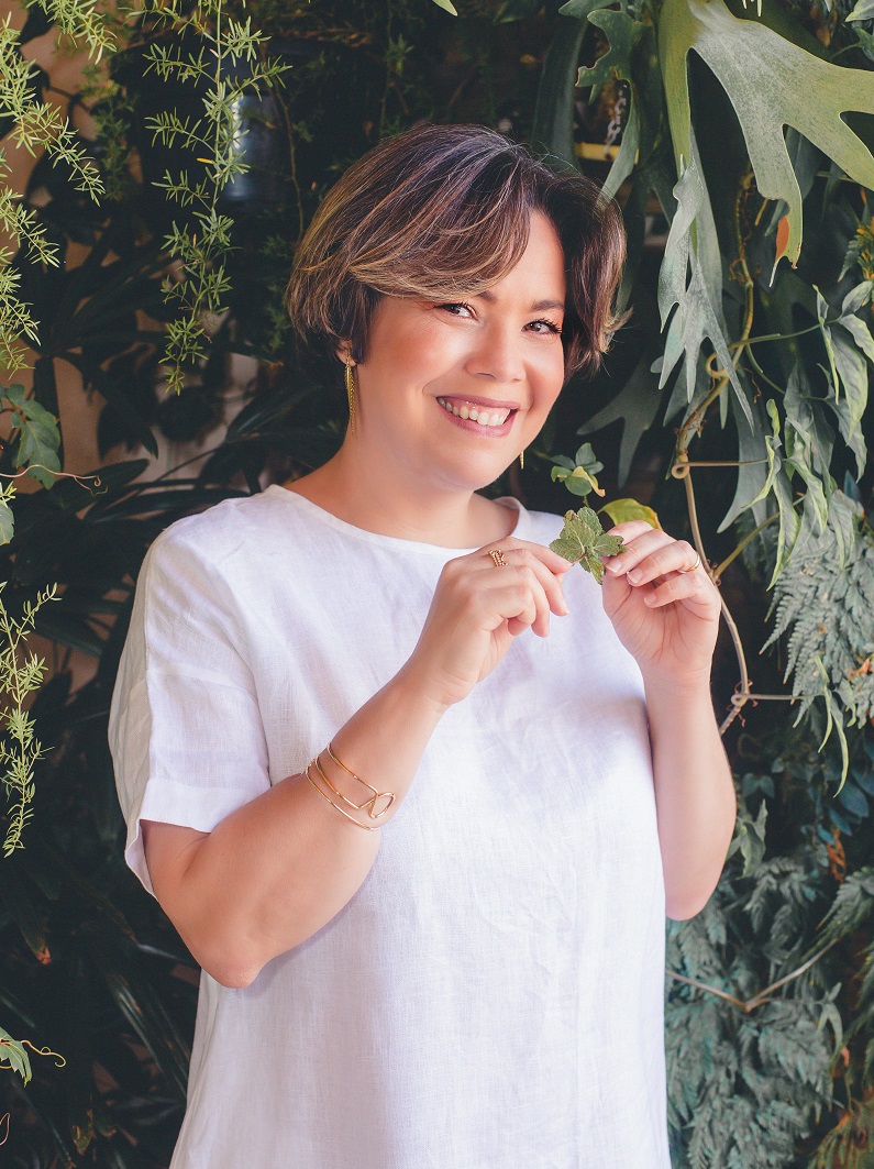 Maria Flávia está em um jardim segurando uma folha