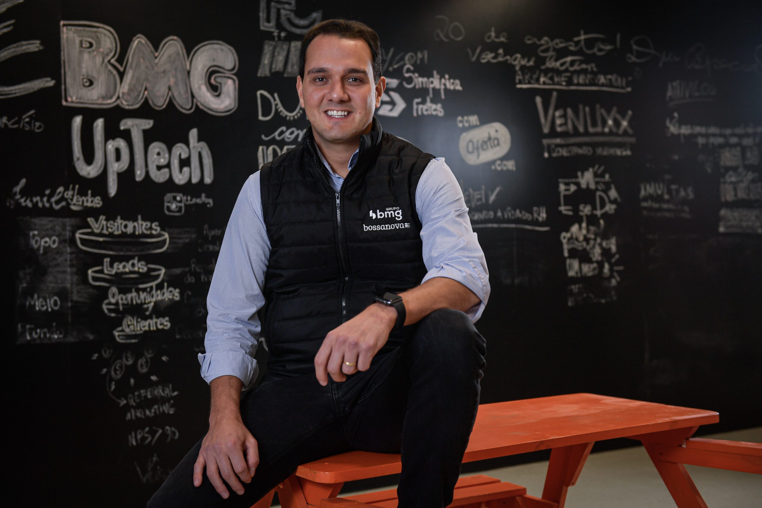 rodolfo está sentado em cima da mesa, olha para frente e sorri